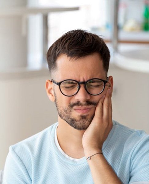 Man holding his cheek and wincing in pain