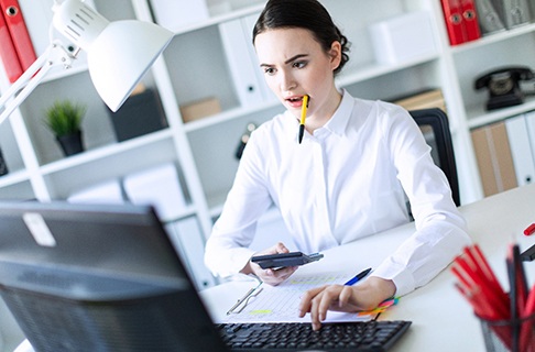 A young female chews on a pen while working on her computer