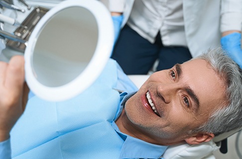 A middle aged man admiring his new smile while at a dental office