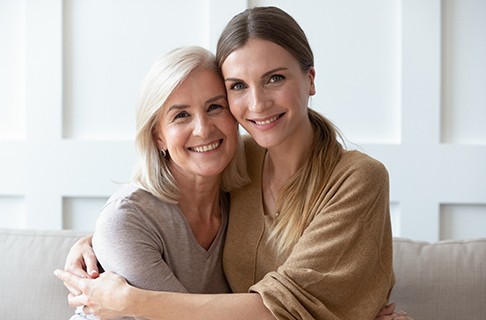 Senior woman and younger woman smiling and hugging on a couch