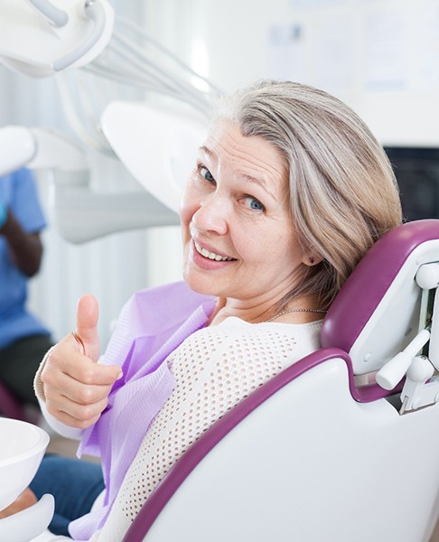 Older woman smiling and giving a thumbs up in the dental chair