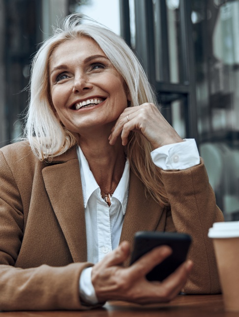 Smiling woman holding her cell phone while sitting at a table
