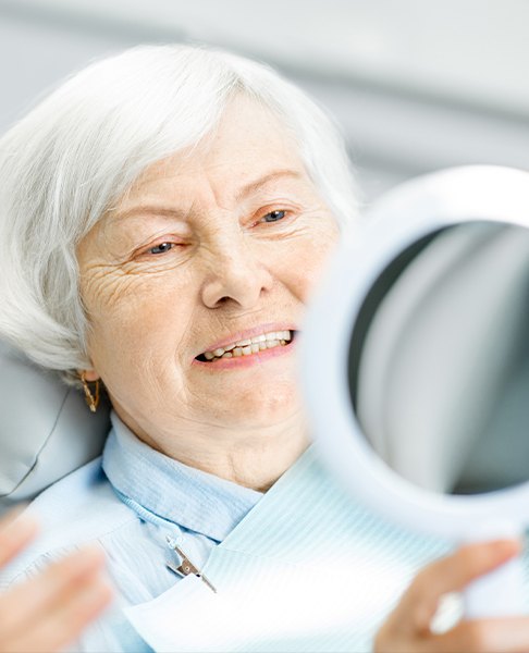 Senior woman looking at her smile in a mirror after pocket reduction surgery