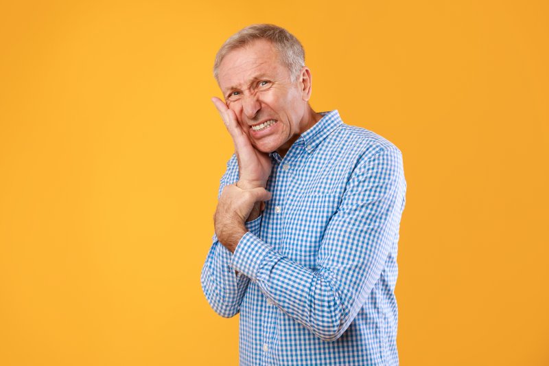 Older patient holding their cheek due to gum disease